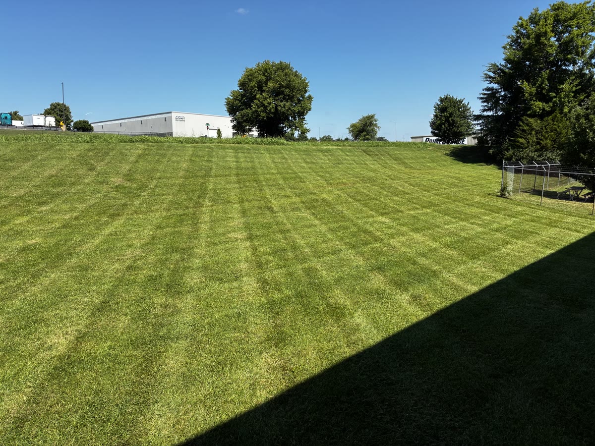 Commercial lawn in front of a white warehouse with a picnic table inside a fenced area.